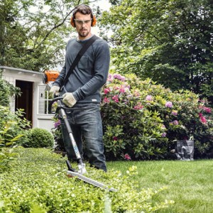 Mężczyzna przycinający żywopłot w ogrodzie przy pomocy Stihl HL-KM 145° Nożyce, przystawka Kombi.