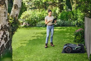 Kobieta sterująca automatyczną kosiarką Stihl iMOW 5 EVO w ogrodzie.