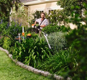 Mężczyzna używający Stihl KMA 80 R, Kombi Motor w ogrodzie pełnym zieleni.