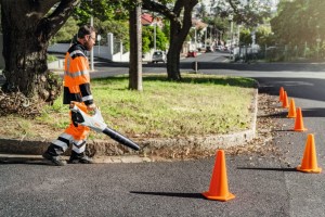 Pracownik w odzieży ochronnej używający Stihl BGA 86 Dmuchawa akumulatorowa na ulicy.