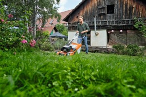 Mężczyzna kosi trawnik przy użyciu kosiarki z napędem Vario Stihl RM 650 V w ogrodzie.