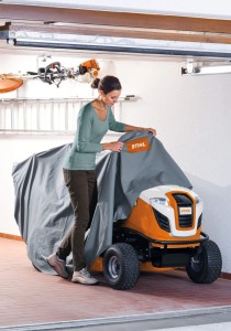 Kobieta nakładająca Stihl AAH 300 Pokrowiec na kosiarkę samojezdną T5 i T6 w garażu.