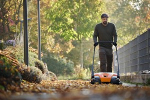 Mężczyzna używający Stihl KG 770 Zamiatarka ręczna do zamiatania liści na alejce w parku.