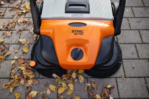 Ręczna zamiatarka Stihl KG 770 na kostce brukowej, otoczona jesiennymi liśćmi.