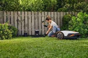 Kobieta instalująca przewód ograniczający Stihl ARB 151 przy robocie koszącym w ogrodzie.