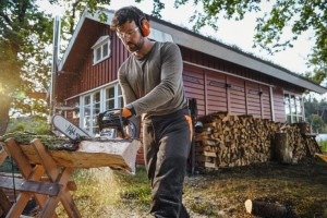 Mężczyzna używający Stihl MS 162 C-BE do cięcia drewna przy domku.