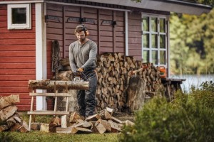 Mężczyzna używa Stihl MS 162 C-BE do cięcia drewna przed czerwoną szopą.