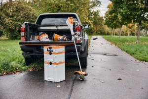 Walizka na akumulatory Stihl Systainer Box System L ustawiona przy otwartym bagażniku samochodu wraz z narzędziami koszącymi.