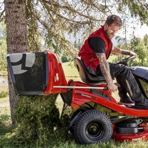 Mężczyzna siedzący na Traktor Alko T18-103.4 HD-A V2 COMFORT w trakcie wyrzucania skoszonej trawy.