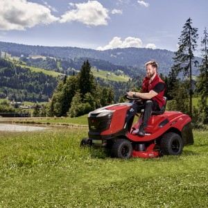 Mężczyzna jadący na czerwonym traktorze ogrodowym Traktor Alko T18-103.4 HD-A V2 COMFORT na tle malowniczego krajobrazu.