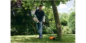 Mężczyzna w ogrodzie używa Stihl FSE 60 Kosa elektryczna do koszenia trawy przy drzewie.