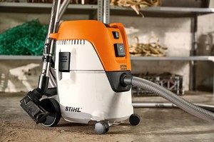 Odkurzacz Stihl SE 62 E do czyszczenia na sucho i mokro z automatycznym włącznikiem na tle półek.