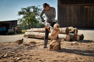 Mężczyzna używający Stihl MS 194 C-E Pilarki spalinowej podczas rzeźbienia drewnianej figury na świeżym powietrzu.