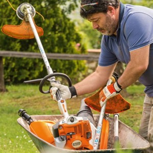 Mężczyzna wkładający Stihl KM 56 RC-E KombiMotor do taczki w ogrodzie.